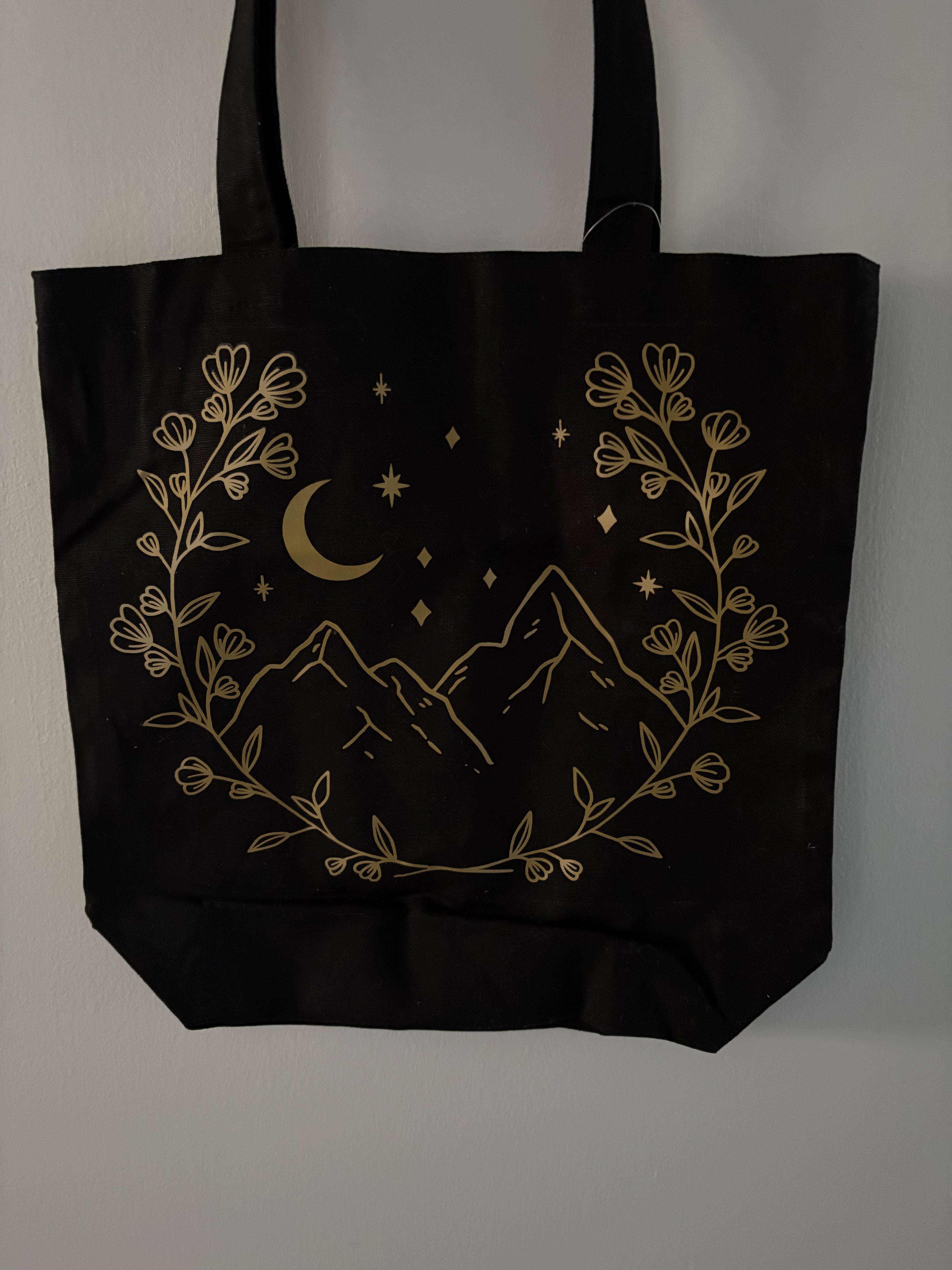 Black tote bag with gold mountain and moon design on a gray background